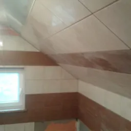 Wykończona łazienka na poddaszu z beżowymi i brązowymi płytkami ceramicznymi ułożonymi w pasy, widoczne okno