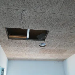 Zamontowany sufit z paneli z włókna drzewnego, z otworem rewizyjnym i otworem na oświetlenie, widoczne kable i białe ściany.