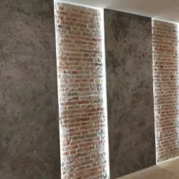 Nowoczesna ściana z panelami z surowej cegły podświetlonymi listwami LED, sąsiadująca z powierzchnią o fakturze betonu architektonicznego.