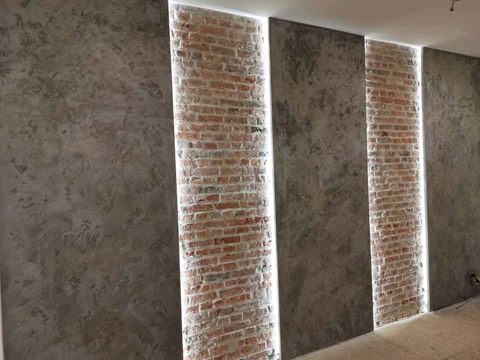 Nowoczesna ściana z panelami z surowej cegły podświetlonymi listwami LED, sąsiadująca z powierzchnią o fakturze betonu architektonicznego.