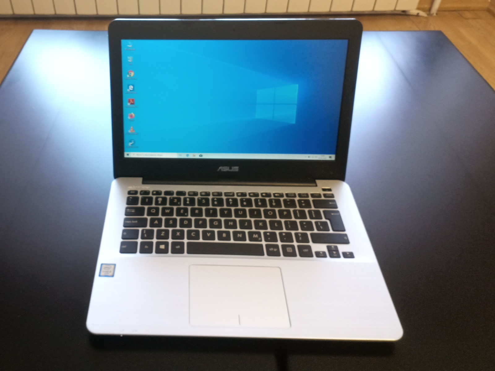 Laptop ASUS z włączonym systemem Windows, widoczne ikony na pulpicie, leżący na ciemnym blacie.