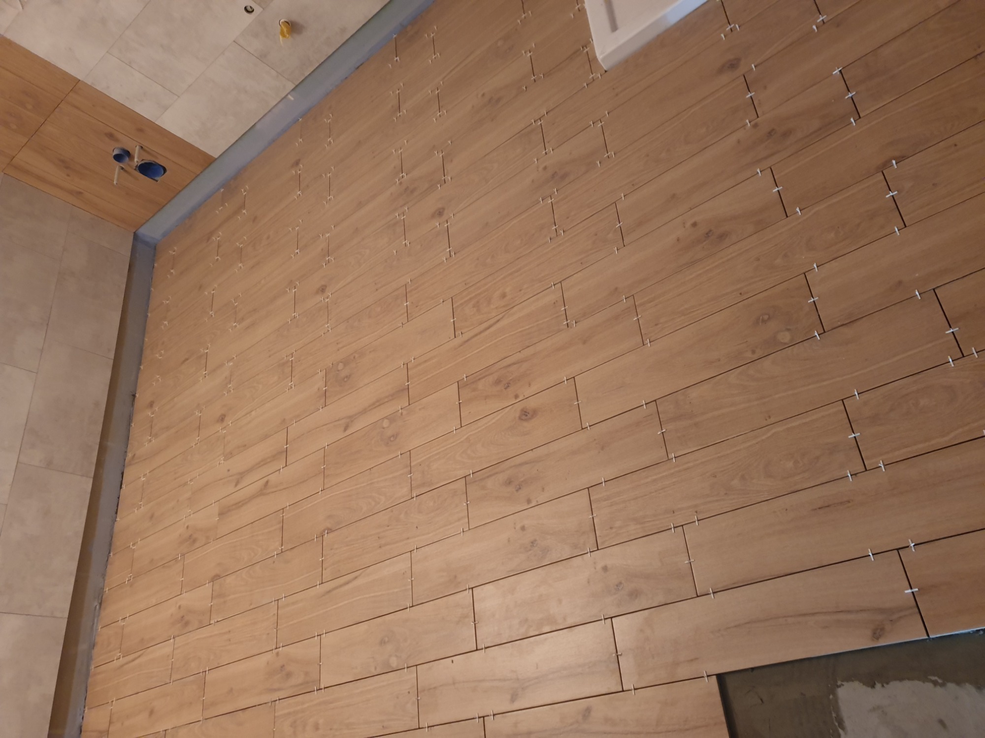 Montaż drewnopodobnych paneli ściennych z białymi krzyżykami dystansowymi w Sztumie, widoczne fragmenty sufitu i podłogi w trakcie prac.