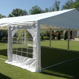 Biały namiot imprezowy z przezroczystymi panelami bocznymi ustawiony na trawniku przed domem z kamienną fasadą.