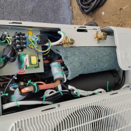 FHU Instur Systemy Grzewcze - Otwarta obudowa klimatyzatora z widocznymi elementami instalacji wewnętrznej, w tym rurami miedzianymi, przewodami elektrycznymi i izolacją, z narzędziami obok sugerującymi prace instalacyjne.