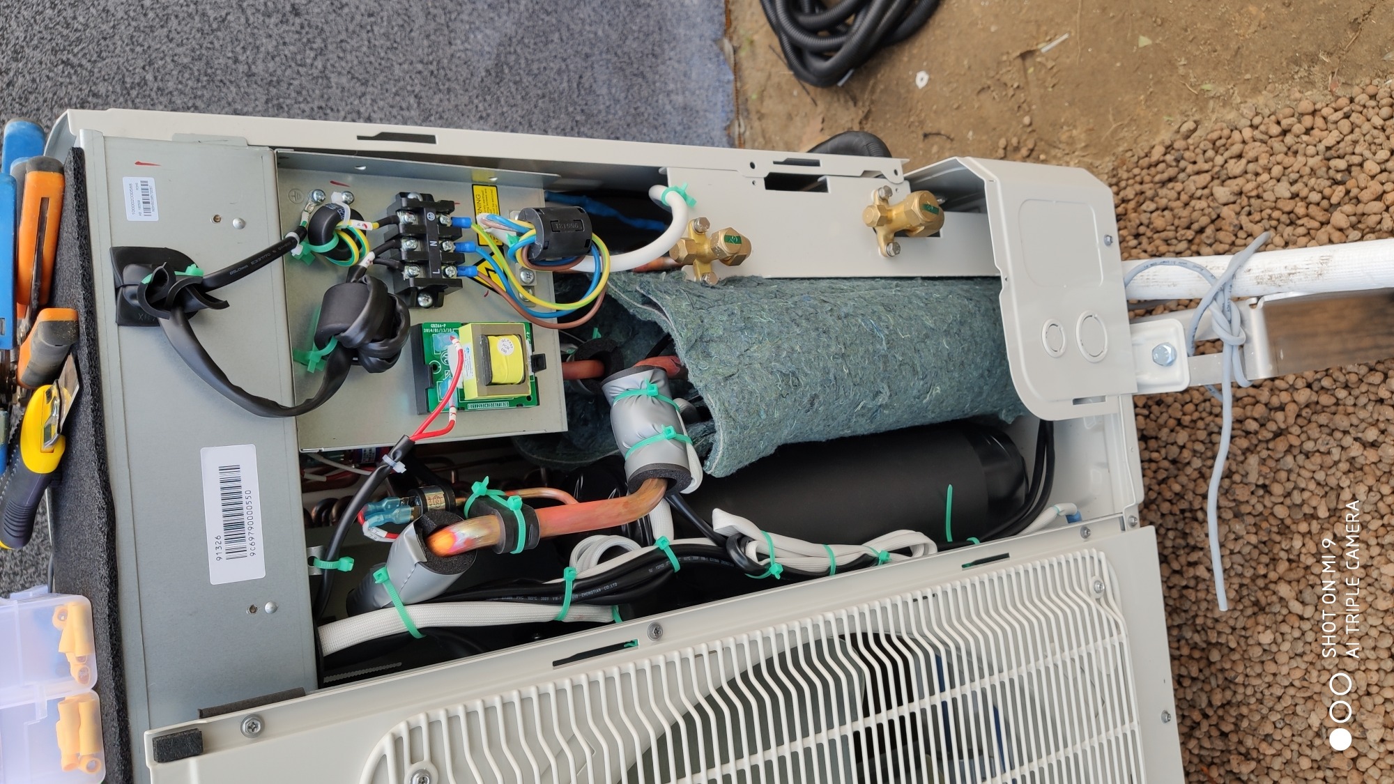 Otwarta obudowa klimatyzatora z widocznymi elementami instalacji wewnętrznej, w tym rurami miedzianymi, przewodami elektrycznymi i izolacją, z narzędziami obok sugerującymi prace instalacyjne.