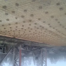 Przygotowanie zbrojenia i deskowania pod wylewkę betonową fundamentu, widoczne siatka zbrojeniowa i dystanse, w tle teren budowy i drzewa.