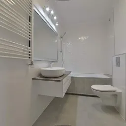 Nowoczesna, jasna łazienka po remoncie w Warszawie, z wiszącą umywalką na szafce, grzejnikiem drabinkowym i toaletą podwieszaną.