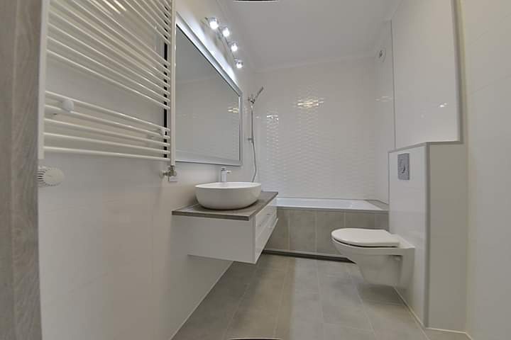 Nowoczesna, jasna łazienka po remoncie w Warszawie, z wiszącą umywalką na szafce, grzejnikiem drabinkowym i toaletą podwieszaną.