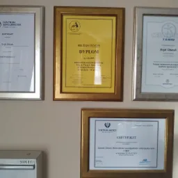 Ściana z czterema oprawionymi certyfikatami i dyplomami potwierdzającymi kwalifikacje zawodowe Eryka Olszaka w zakresie terapii manualnej, suchego igłowania, terapii mięśniowo-powięziowych...