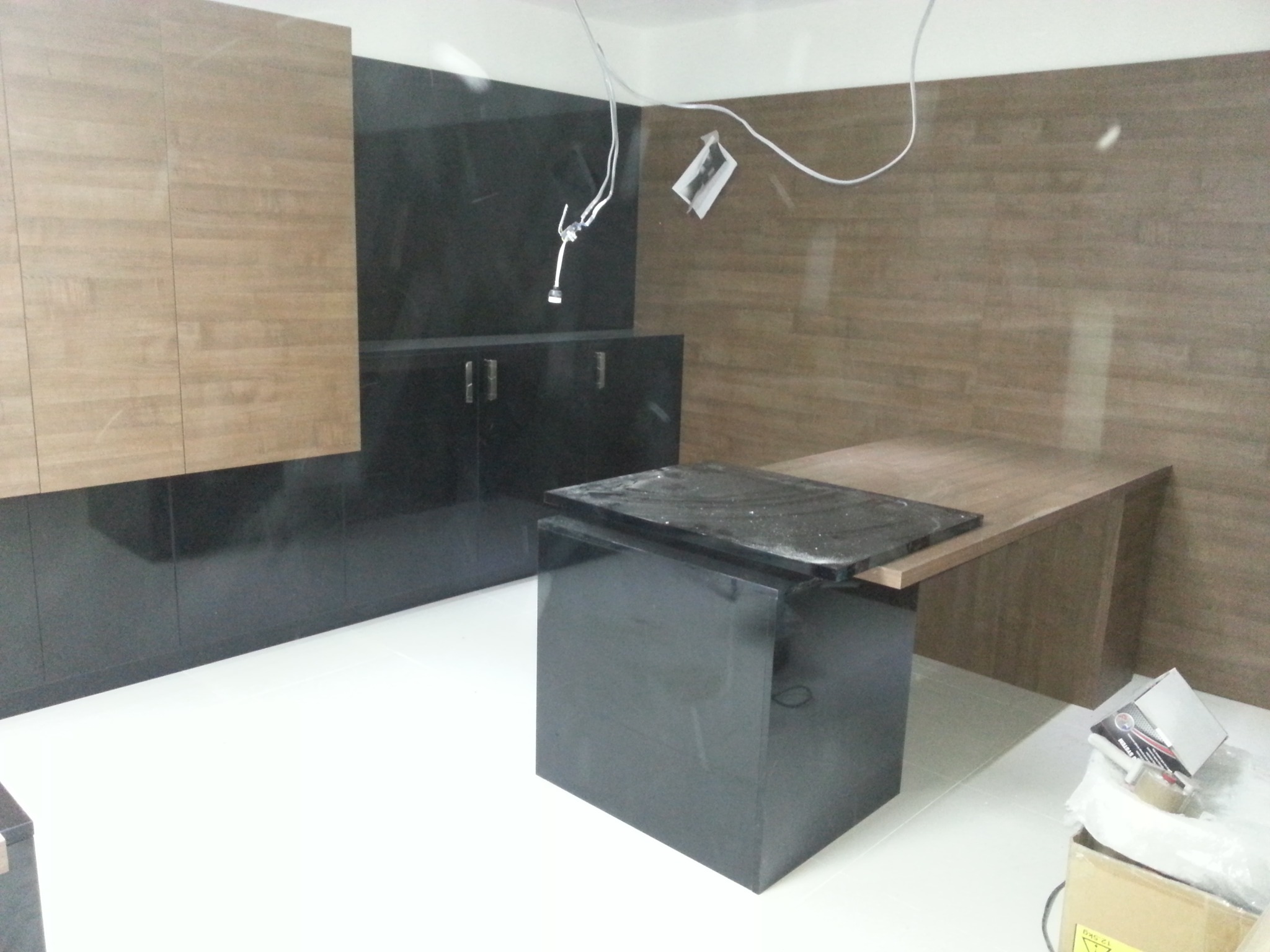 Wnętrze łazienki w trakcie prac wykończeniowych: widoczne czarne szafki z połyskiem, drewnopodobne panele na ścianach, biała podłoga oraz przygotowany blat z czarnego kamienia.