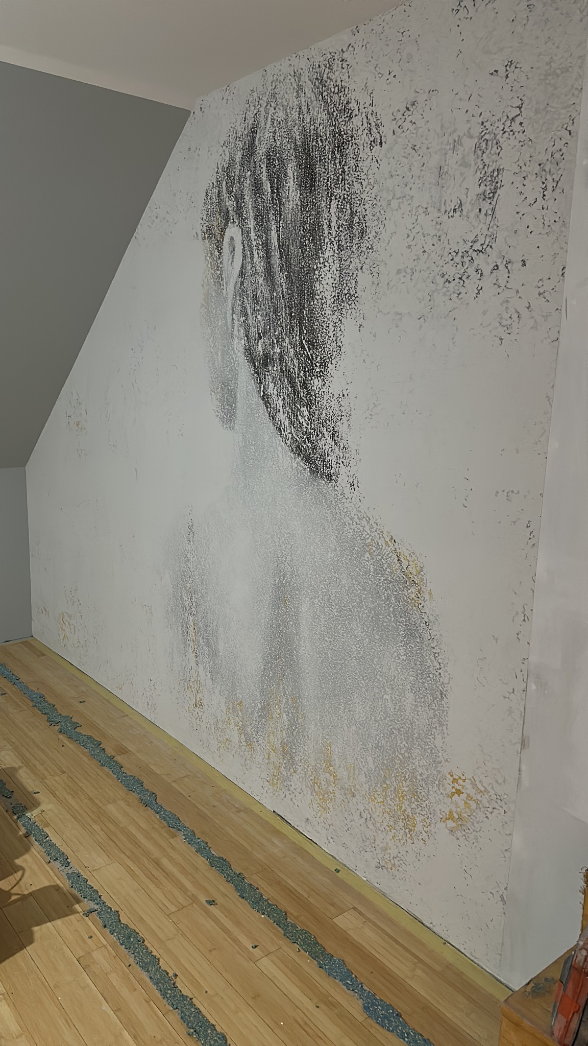 Ściana w pokoju na poddaszu z dekoracyjną, artystyczną fakturą imitującą rysunek postaci. Podłoga zabezpieczona folią malarską. Ujęcie z dołu, z boku.