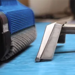 Szczegółowe ujęcie szczotki i ssawki odkurzacza piorącego na niebieskiej powierzchni, widoczny fragment urządzenia z niebieskim elementem obudowy i szare włosie szczotki.