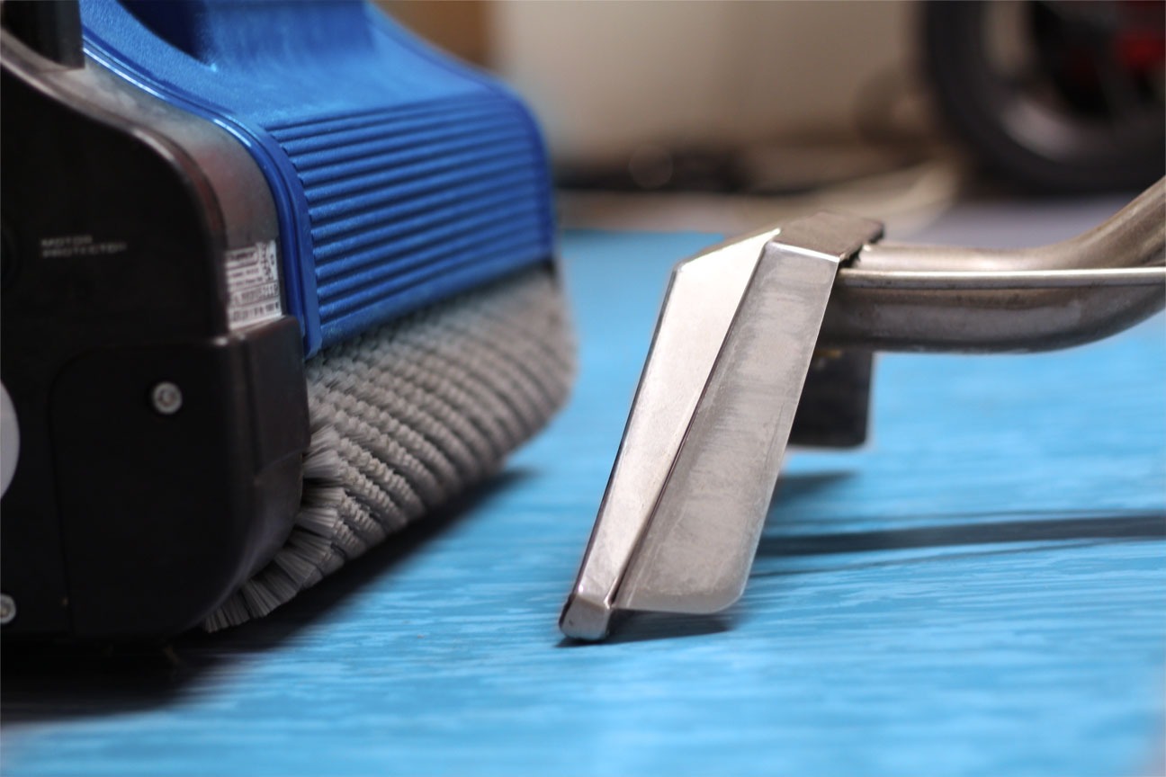 Szczegółowe ujęcie szczotki i ssawki odkurzacza piorącego na niebieskiej powierzchni, widoczny fragment urządzenia z niebieskim elementem obudowy i szare włosie szczotki.