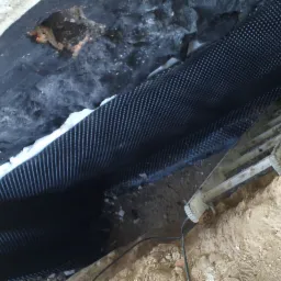 Czarna folia kubełkowa z białą pianką na fundamencie, widoczna drabina i wykop ziemny.