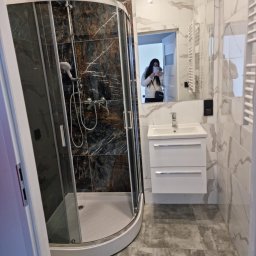 Abecedarian-bud - Nowoczesna łazienka z kabiną prysznicową typu walk-in, umywalką z szafką i marmurowymi płytkami na ścianach; odbicie osoby robiącej zdjęcie w lustrze.