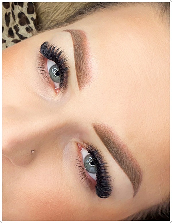 Zbliżenie na twarz kobiety po zabiegu stylizacji brwi metodą pudrową i przedłużania rzęs, widoczne pełne, ciemne rzęsy i symetryczne, brązowe brwi, delikatny makijaż.