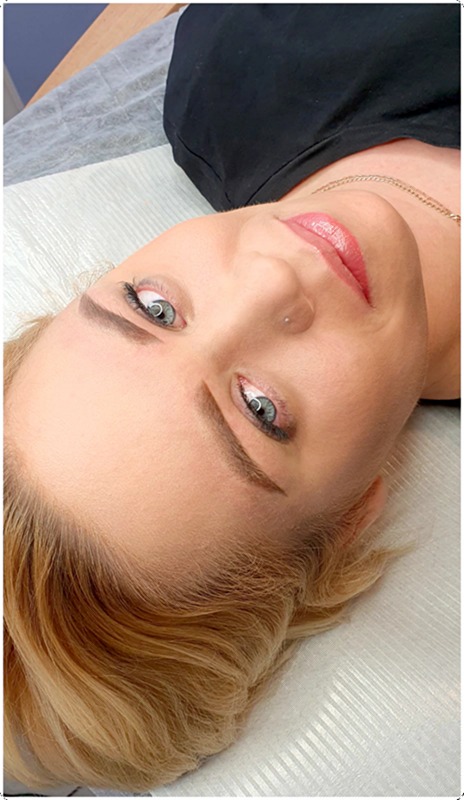 Portret kobiety po zabiegu makijażu permanentnego brwi i ust, widoczne świeżo wykonane brwi i delikatny błyszczyk na ustach, z pierścionkiem w nosie.