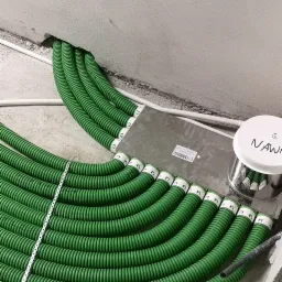 Układanie zielonych, karbowanych rur wentylacyjnych w nowym budynku, z widoczną puszką instalacyjną i metalową listwą montażową.