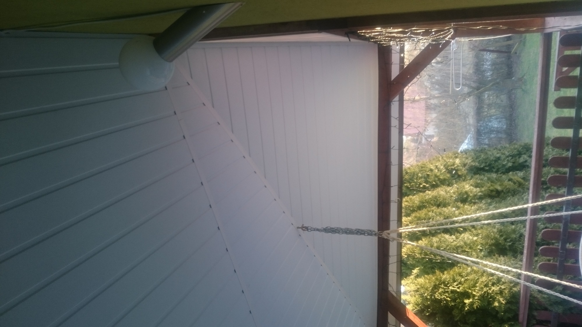 Biała podbitka dachowa z widocznym systemem odwadniania, uchwycona z perspektywy żabiej, z fragmentem ogrodu w tle.