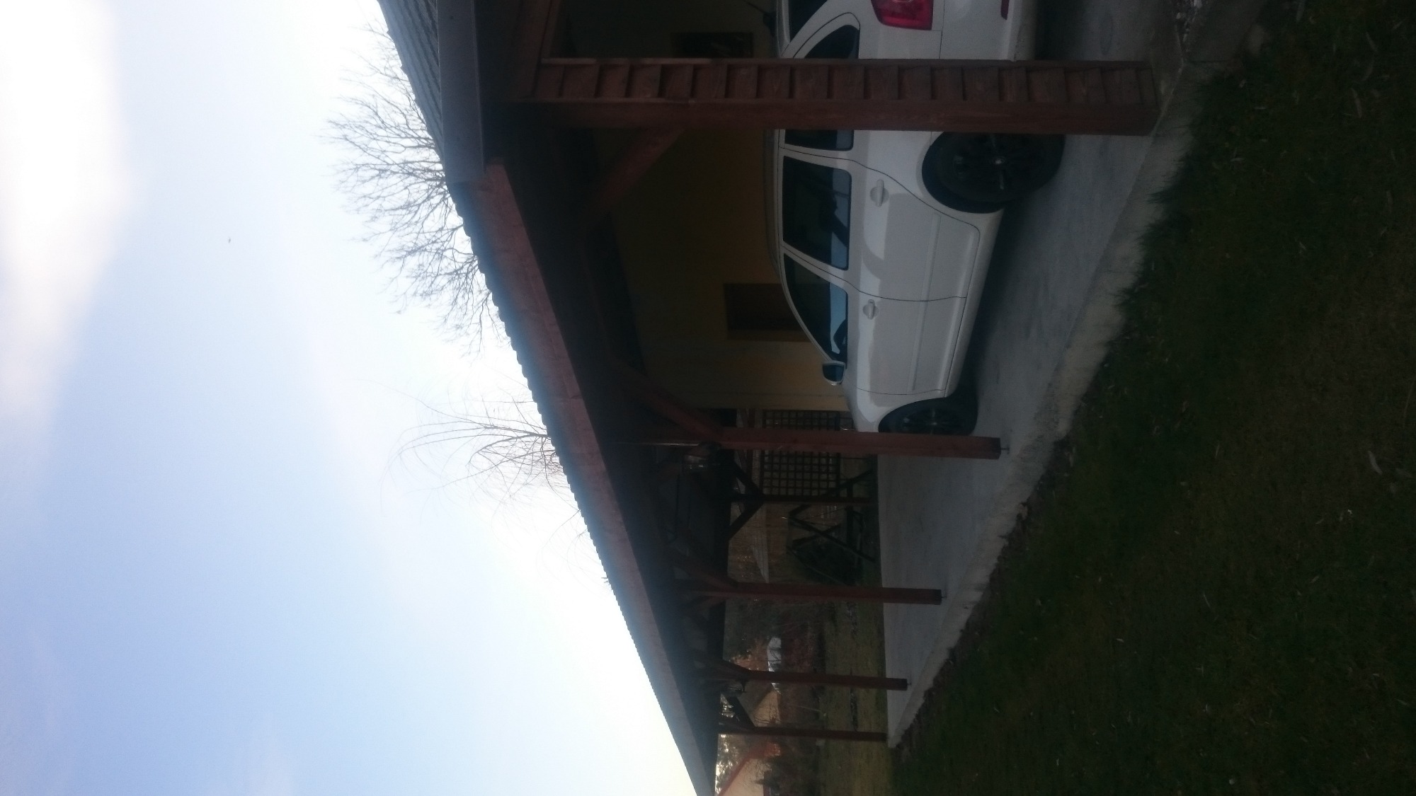 Zadaszenie wiaty garażowej z drewnianą konstrukcją i widocznym fragmentem dwóch białych samochodów na betonowej posadzce.