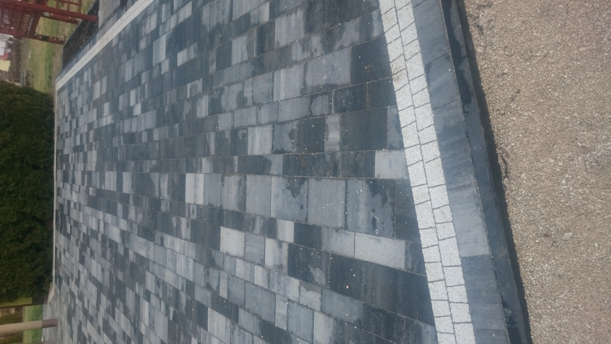Ułożona nawierzchnia z szarych kostek brukowych, obrzeżona jasnymi kostkami, widok z góry, obok wysypany żwir.