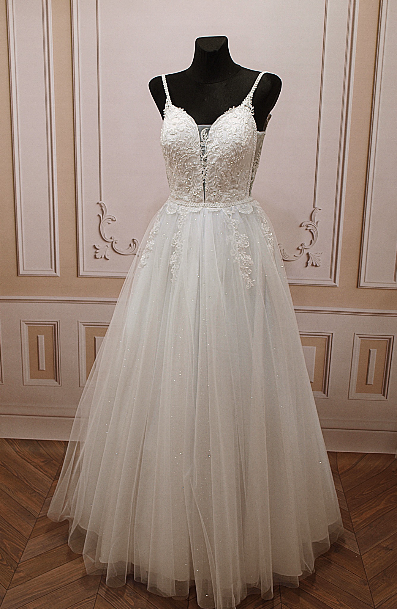 Elegancka suknia ślubna z koronkowym gorsetem i tiulową spódnicą, prezentowana na manekinie na tle dekoracyjnej ściany.