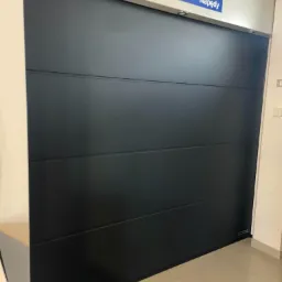 Zamknięta, czarna brama z poziomymi panelami, marki Hormann, oświetlenie punktowe na górze, widoczny fragment podłogi z płytek.