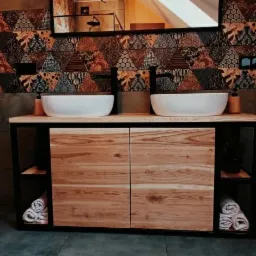 Szafka łazienkowa z dwiema umywalkami nablatowymi, stalowy profil ramy wykończony czarnym lakierem proszkowym, fronty z drewna jesionowego pokryte bezbarwnym lakierem akrylowym, na tle ściany...