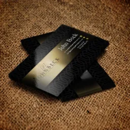 Stos wizytówek z czarnym geometrycznym wzorem i złotym paskiem z logo 'John Beck Personalised Wedding Entertainment' na tle jutowego worka.