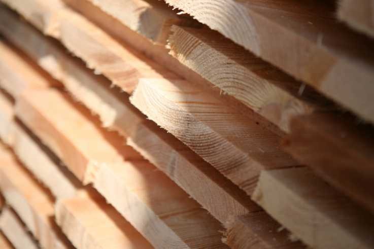 Stos świeżo przetartego drewna iglastego ułożonego pod kątem, widoczne słoje i jasne drewno.