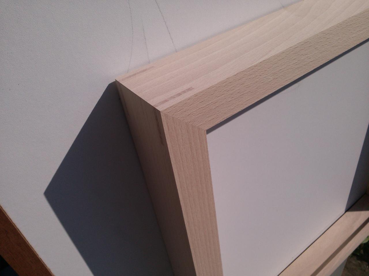 Detale drewnianej ramy okiennej w jasnym odcieniu, widoczne połączenia stolarskie. Oświetlenie słoneczne podkreśla fakturę drewna i geometrię konstrukcji.