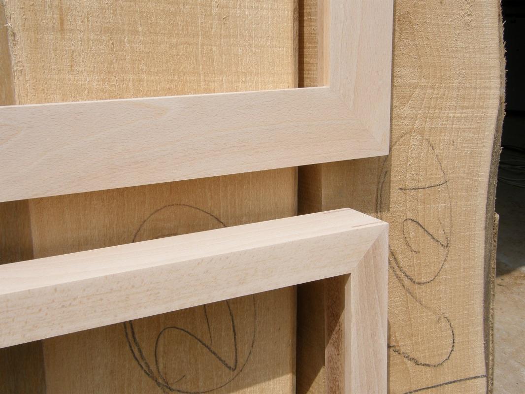 Surowe, jasne drewniane ramy okienne ułożone na stosie desek z widocznymi śladami ołówka.