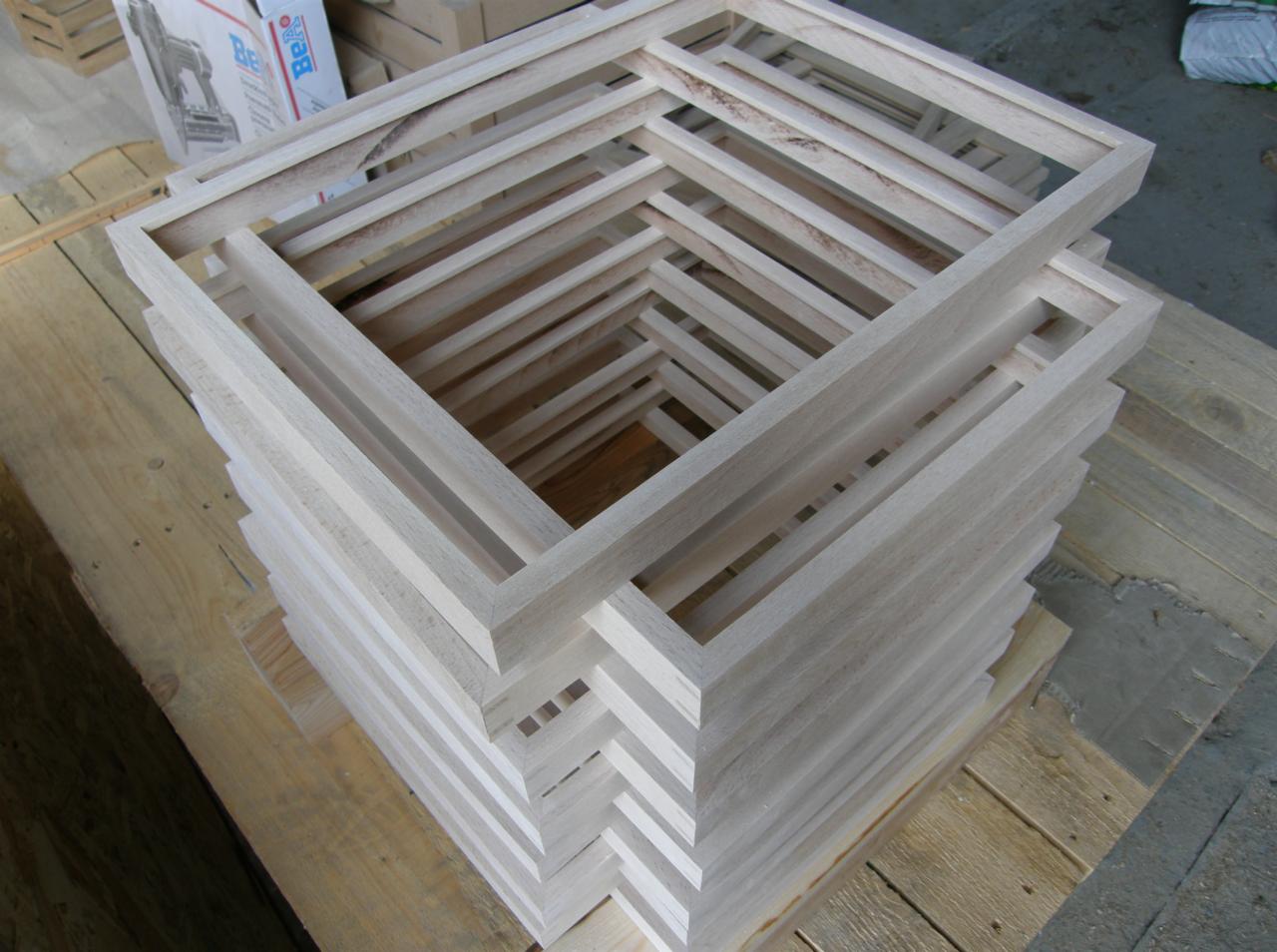 Stos surowych, drewnianych ramek okiennych ułożonych na drewnianej palecie, widoczne słoje drewna i niedoskonałości obróbki.