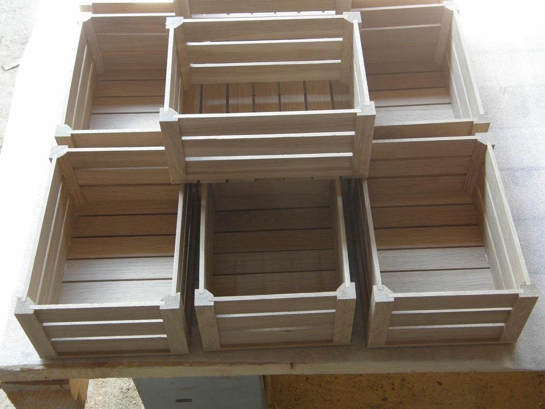 Ręcznie wykonane, drewniane skrzynki ogrodowe z jasnego drewna, ułożone w stos, widoczne detale łączeń narożnych.