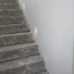 Betonowe schody z wbudowanymi, okrągłymi lampkami LED w ścianie, oświetlającymi stopnie.