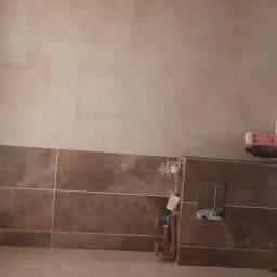 Luxbud - Wykończona łazienka z beżowo-brązowymi płytkami, białą wanną i toaletą; widoczne akcesoria łazienkowe i oświetlenie.