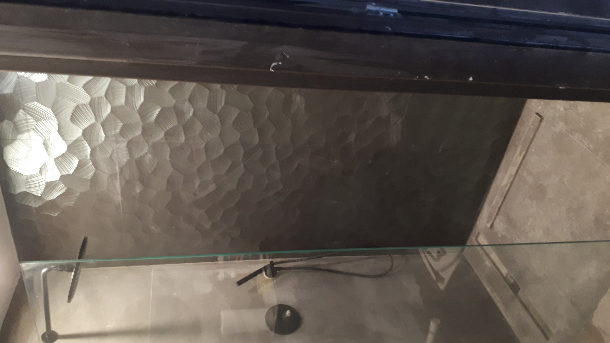 Szara ściana w kabinie prysznicowej z wyraźną fakturą, widoczna przez szklaną szybę kabiny.