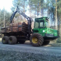 Zielony forwarder z załadowanym drewnem sosnowym na leśnej drodze, widoczne duże opony z żółtymi felgami i wysięgnik żurawia.