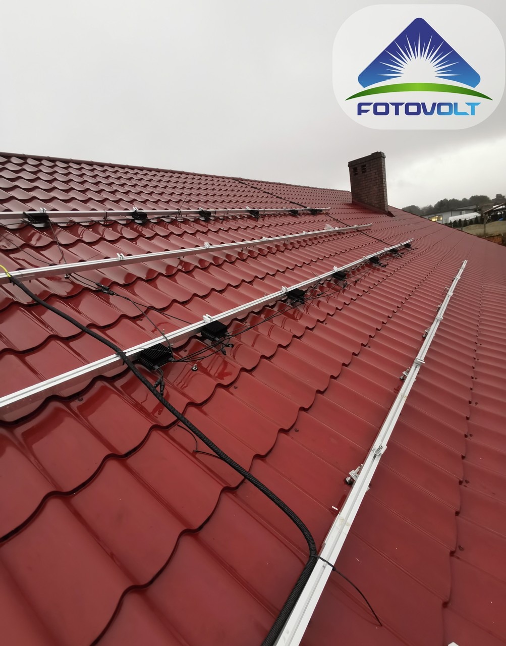 Montaż stelażu pod panele słoneczne na czerwonym dachu z dachówki ceramicznej, widok z dołu pod kątem, pochmurna pogoda.