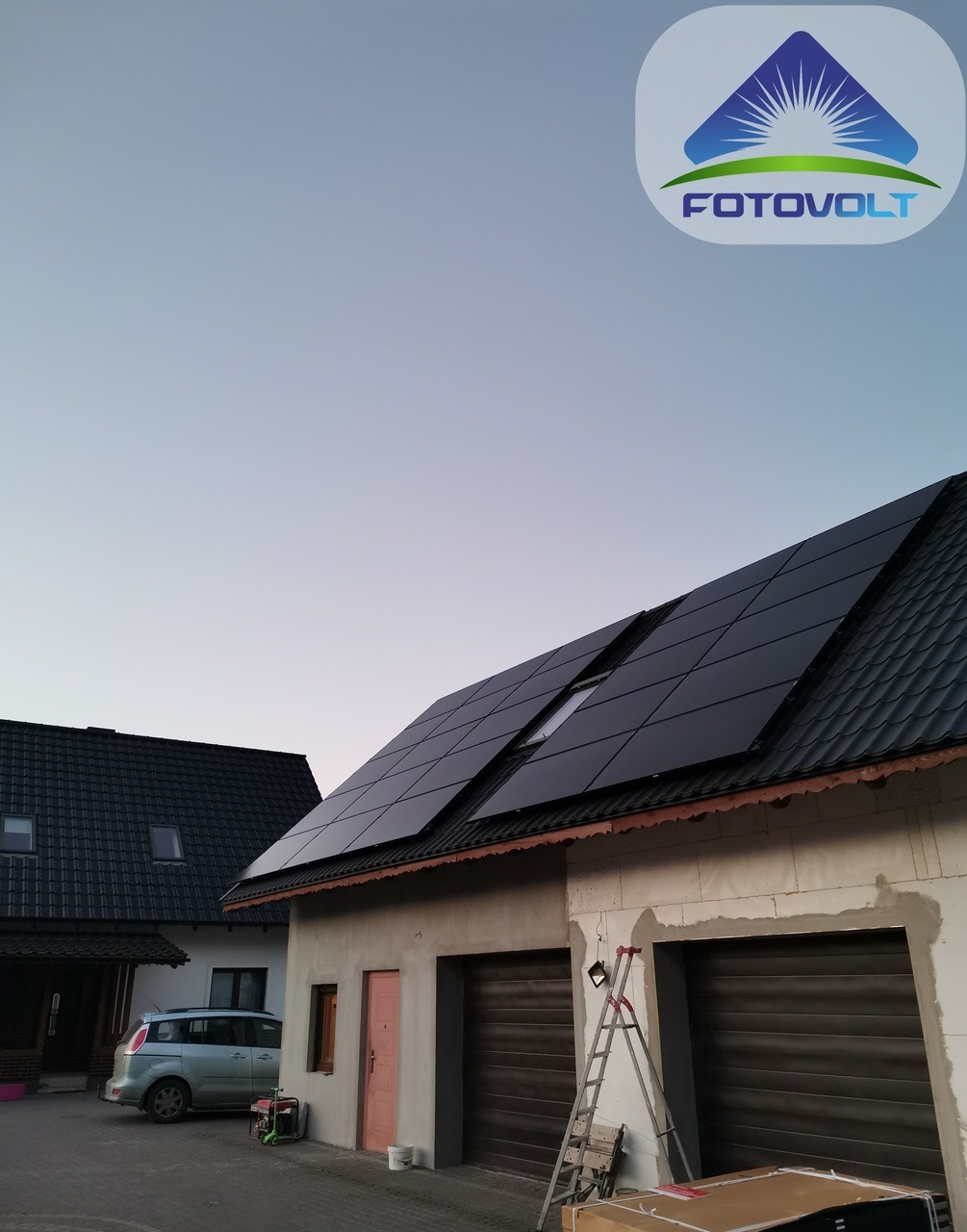 Czarny panel słoneczny na dachu domu jednorodzinnego w trakcie montażu, widoczna drabina oparta o ścianę budynku, w tle zaparkowany samochód i logo firmy w rogu.