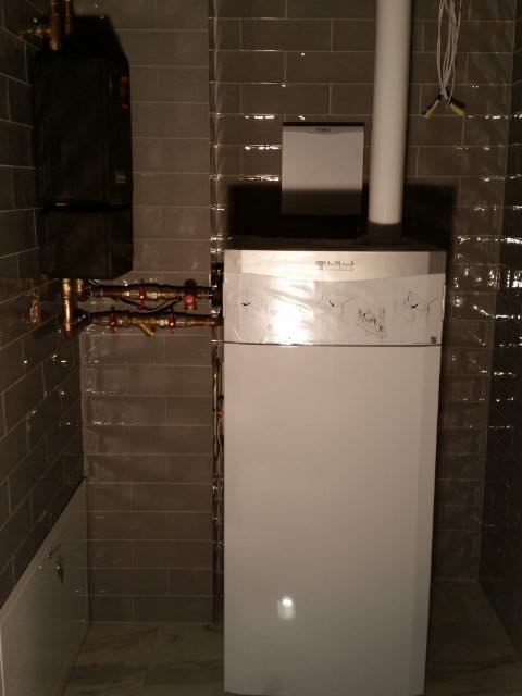 Zdjęcie przedstawia zamontowany dwufunkcyjny kocioł gazowy marki Vaillant w łazience wykończonej szarą glazurą w Szczecinie, widoczne rury i elementy instalacji.