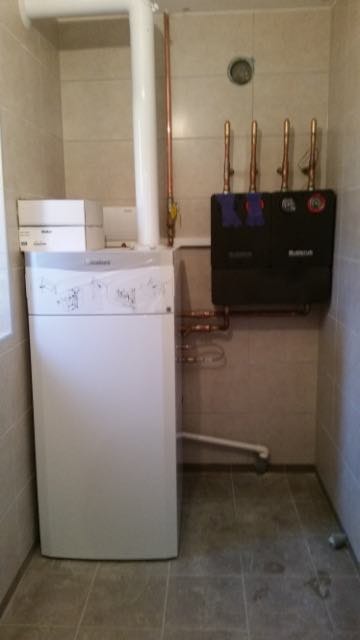 Biały piec gazowy z czarną skrzynką Buderus na ścianie w pomieszczeniu wyłożonym płytkami.