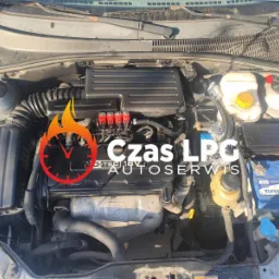 Silnik samochodu z instalacją LPG, widoczne czerwone wtryskiwacze, akumulator Varta, warsztat w Warszawie.