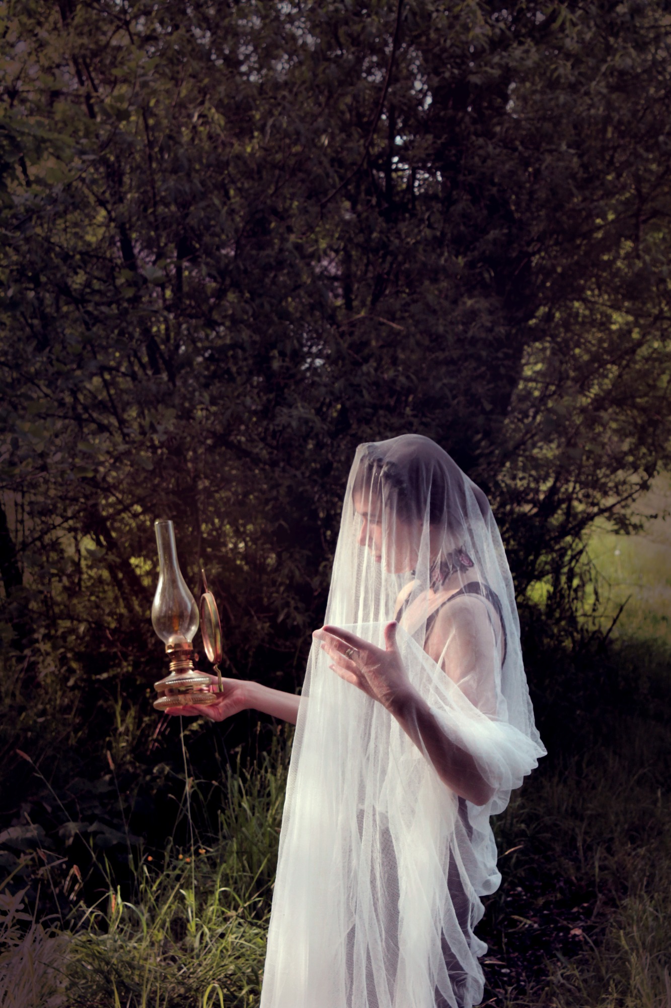 Kobieta okryta woalką trzyma lampę naftową na tle zieleni