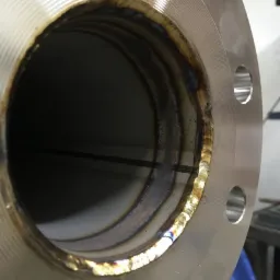 Wewnętrzny spaw okrągłego metalowego kołnierza z widocznymi warstwami spoiny i przebarwieniami termicznymi, minimalne odpryski spawalnicze na powierzchni kołnierza.