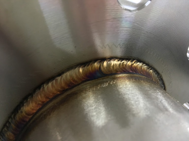 Szczegółowe zbliżenie na estetyczne połączenie spawane dwóch elementów metalowych, widoczne ślady termiczne i precyzyjny szew.