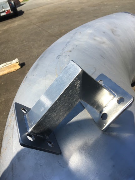 Metalowa konstrukcja wspornikowa, spawana do rury o dużym przekroju, z widocznymi otworami montażowymi na kwadratowych podstawach, wykonana ze stali nierdzewnej, z delikatnymi śladami spawania.