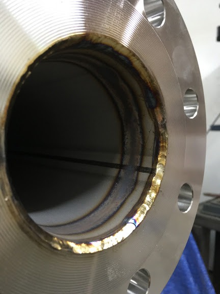 Wewnętrzny spaw okrągłego metalowego kołnierza z widocznymi warstwami spoiny i przebarwieniami termicznymi, minimalne odpryski spawalnicze na powierzchni kołnierza.