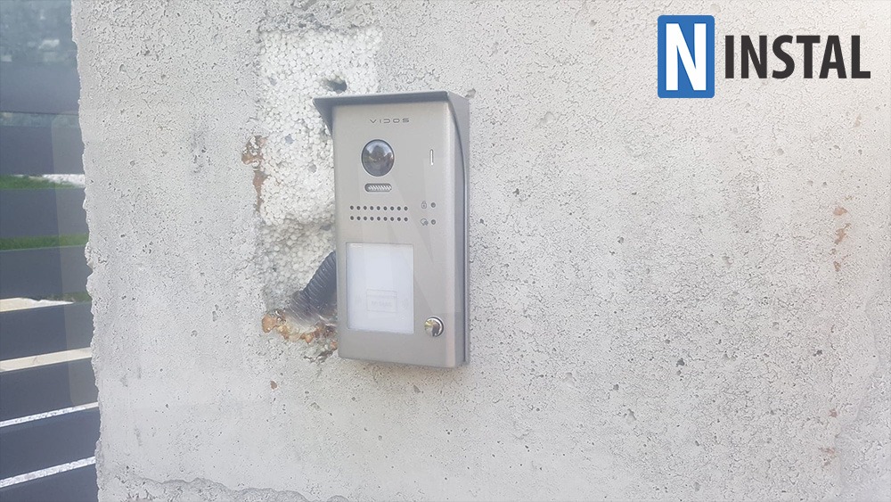 Zamontowany wideodomofon Vidos na szarej, surowej ścianie z widocznymi śladami po instalacji, obok logo firmy N Instal.