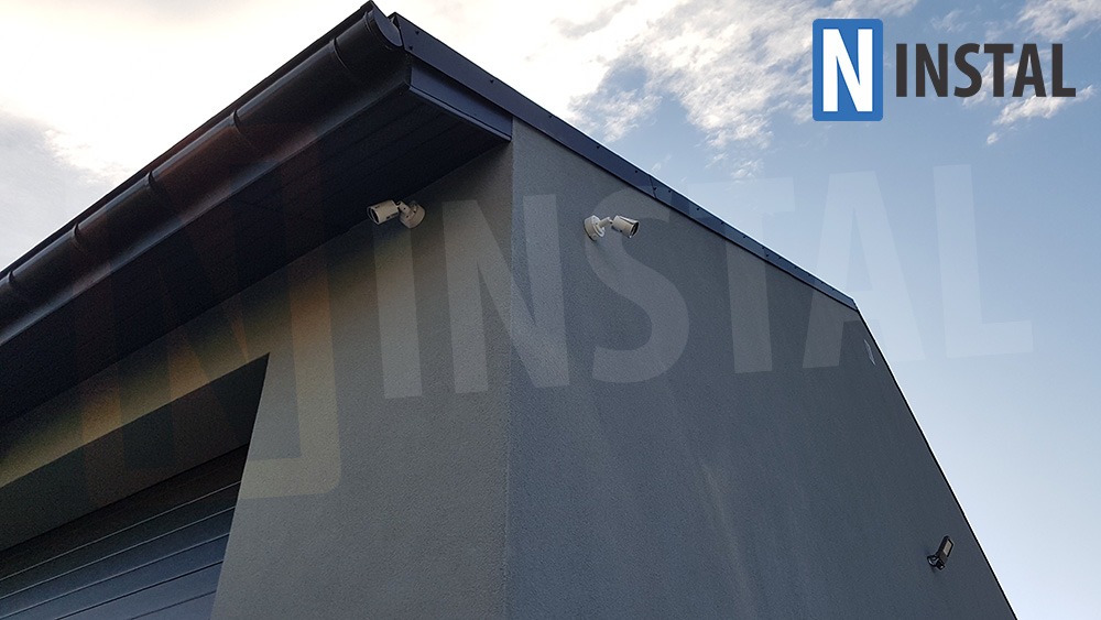 Zewnętrzny montaż dwóch kamer monitoringu na ścianie budynku w Goleszowie, widok z dołu, z logo firmy w prawym górnym rogu.